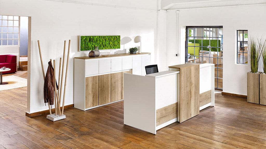 Heller Empfangsbereich mit einer Kombination aus weißen und holzfarbenen Möbeln, grüner Wanddekoration und Holzboden.