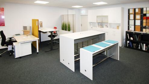 Zwei weiße Stehtische vor weißen Schreibtischen auf grauem Teppich