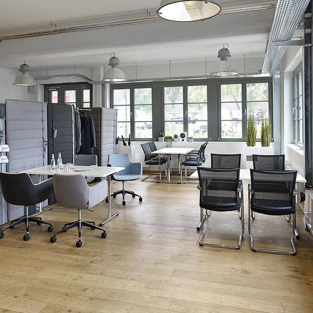 Einzelne Tische im Cafeteria-Bereich mit dunklen Stühlen und Holztischen