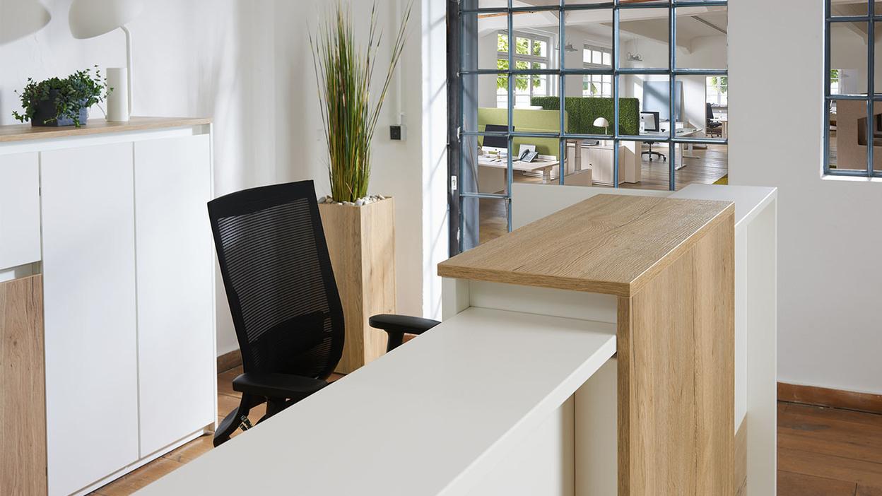 Tresenelement mit weiß-brauner Front Tresenelement aus weißem Holz mit Holzelement vor schwarzem Schreibtischstuhl