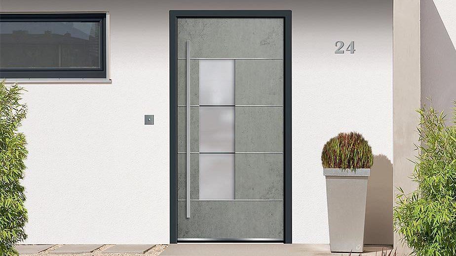 Graue Haustür in Betonoptik mit schwarzem Rahmen vor weißer Wand