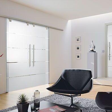 Stilvoller Wohnraum mit modernen Glastüren nach Maß. Eine großflächige Schiebetür mit satinierten Glasflächen und Edelstahlgriffen trennt den Raum optisch, während die gegenüberliegende Eingangstür mit ä