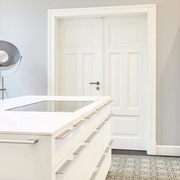 Elegante, doppelflügelige Tür nach Maß in Weiß mit klassischem Kassettendesign, eingebettet in eine moderne, helle Küche mit stilvoller Einrichtung. Die Tür verleiht dem Raum eine hochwertige und zeitlose Optik.
