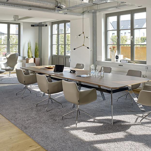 Langer Konferenztisch mit acht Plätzen vor Sprossenfenstern