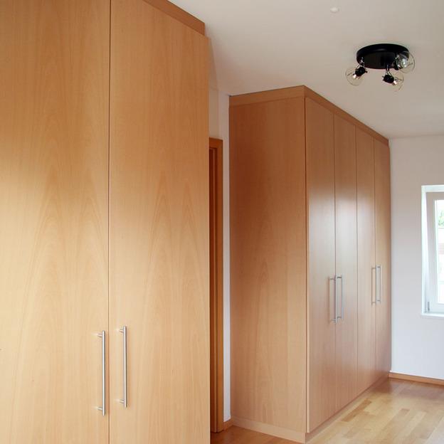 Ein langer, hellholzfarbener Einbauschrank, der als Regal nach Maß in einem Flur dient, optimal genutzt für Stauraum und Ästhetik in einem modernen Wohnraum.