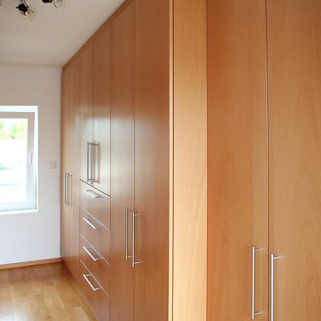 Ein perfekt in den Raum integriertes Regal nach Maß mit Schubladen und Schränken in einem hellen Holzton, das Harmonie und Ordnung in einen modernen Wohnbereich bringt.