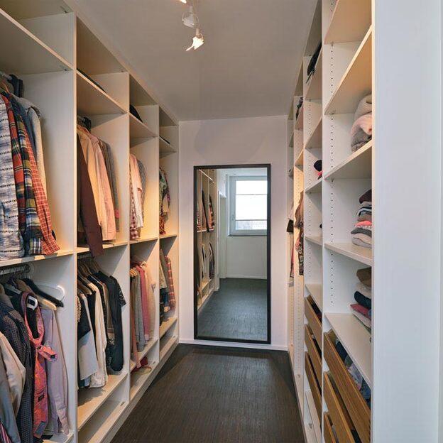 Ein gut organisierter begehbarer Kleiderschrank mit zahlreichen Regalen und Kleiderstangen, gefüllt mit ordentlich arrangierter Kleidung und Accessoires.