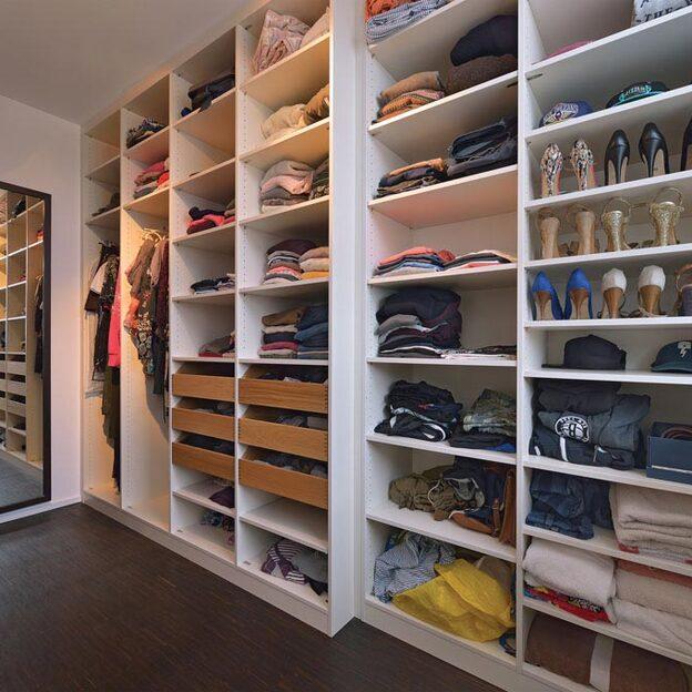 Ein einladender begehbarer Kleiderschrank mit offenen Regalen und Kleiderstangen, prall gefüllt mit Kleidung, Schuhen und Accessoires, beleuchtet durch natürliches Licht.