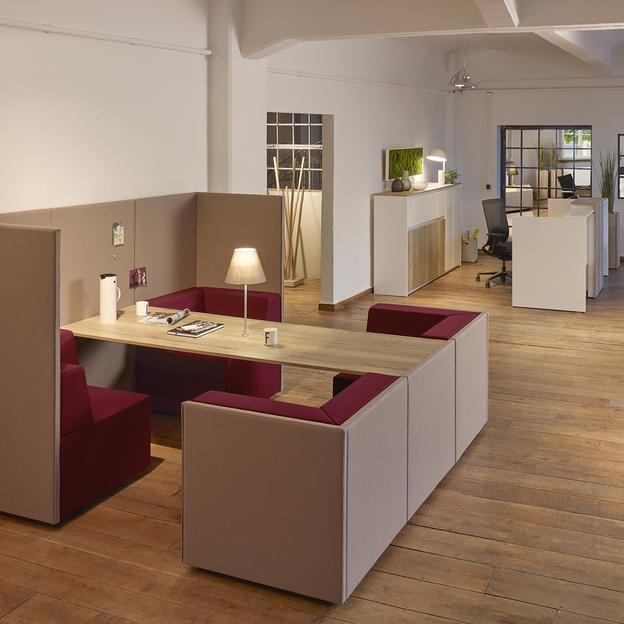 Modern gestaltetes Büro mit integrierten Sitzmöbeln eitläufiges Büro mit eleganten, in Grau und Bordeaux gehaltenen Sitzmöbeln, umgeben von weißen Wänden und hohen Decken, beleuchtet durch sanfte Stehleuchten.