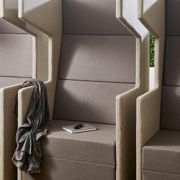 Modernes Sitzmöbel mit geometrischen Mustern Detailansicht eines modernen Sitzmöbels in Grau mit geometrischen Ausschnitten, die natürliche Beleuchtung bieten, und einer stilvollen grauen Schaldekoration.