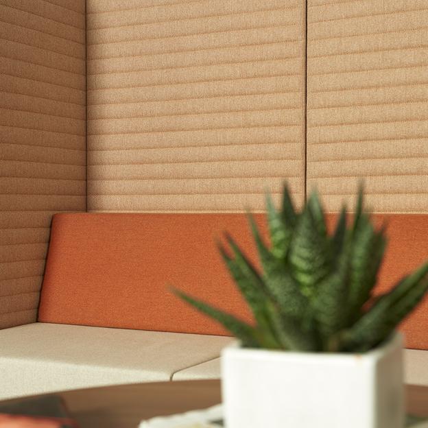 Gemütliche Ecke mit Sitzmöbel in warmen Farbtönen Nahaufnahme eines Sitzmöbels in Beige und Orange, ergänzt durch eine grüne Topfpflanze, die Farbe und Leben in die gemütliche Ecke bringt.