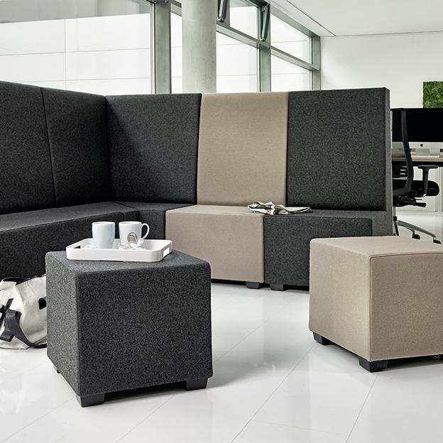 Modernes Bürolayout mit vielseitigen Sitzmöbeln Eine Gruppe moderner Sitzmöbel in einem minimalistischen Büro mit glänzendem Boden und großen Fenstern, bestehend aus hohen Trennwänden und modularen Hockern in Grau- und Beigetönen.