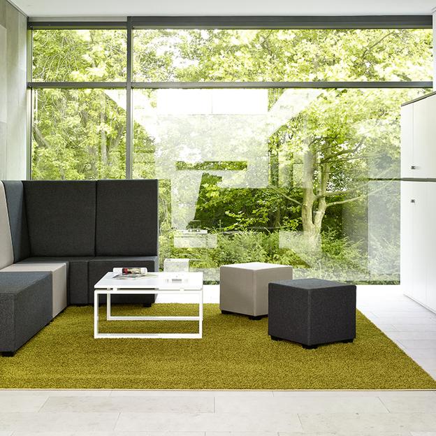 Modernes Büro mit Blick auf den Garten Ein Büro mit großen Fenstern, durch die ein Garten zu sehen ist. Es enthält moderne Sitzmöbel auf einem grünen Teppich, neben einer stilvollen Stehlampe und weißen Schränken.