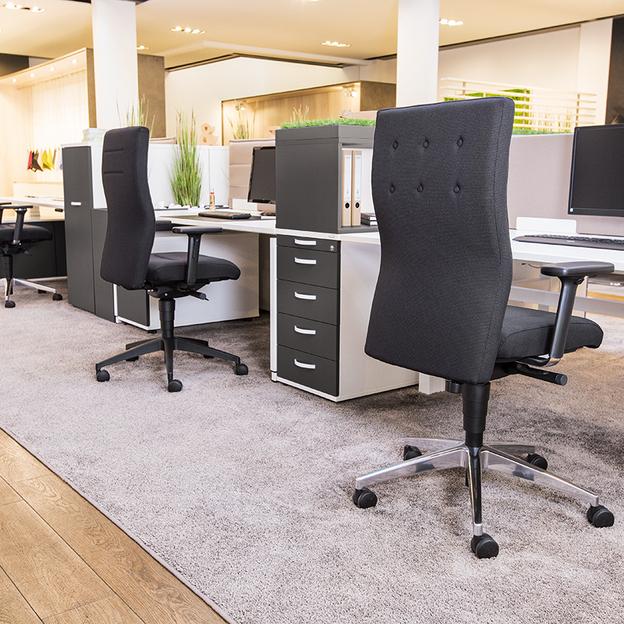 Moderne Büroeinrichtung mit ergonomischen Stühlen Ein helles Büro mit mehreren ergonomischen Sitzmöbeln in Schwarz, arrangiert um Arbeitsplätze mit weißen Tischen, umgeben von dekorativen Grünpflanzen und einem weichen Teppich.