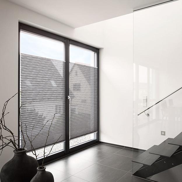 Plissee-Vorhänge mit feiner Struktur als Sonnenschutz an großflächiger Fensterfront im Wohnbereich
