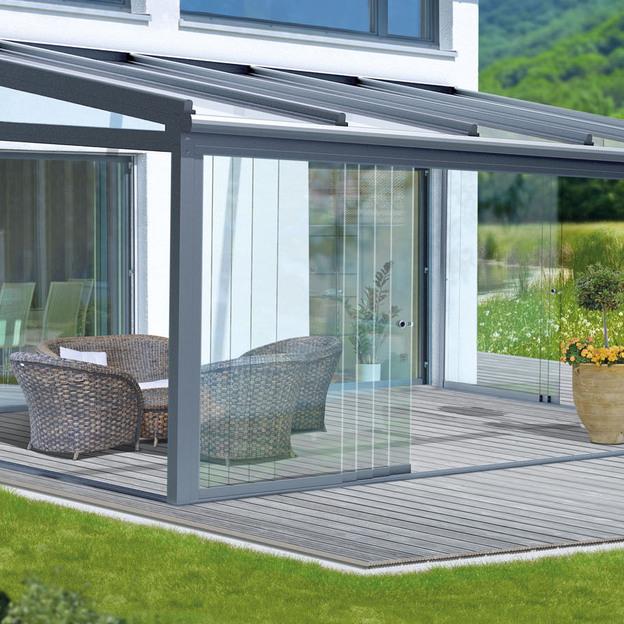 Modernes Haus mit Vordach und Schiebetüren Moderne Schiebetürsysteme mit Vordach verbinden einen stilvollen Innenraum mit einer grünen Außenlandschaft. Komfortable Sitzgelegenheiten und eine Holzterrasse bieten einen entspannenden Blick ins Grüne.