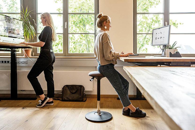 Höhenverstellbare Schreibtische Zwei Frauen vor Schreibtischen in unterschiedlicher Höhe – stehend und sitzend
