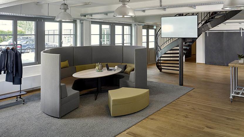 Grauer Loungebreich rund um einen Holztisch vor Treppe im Raum